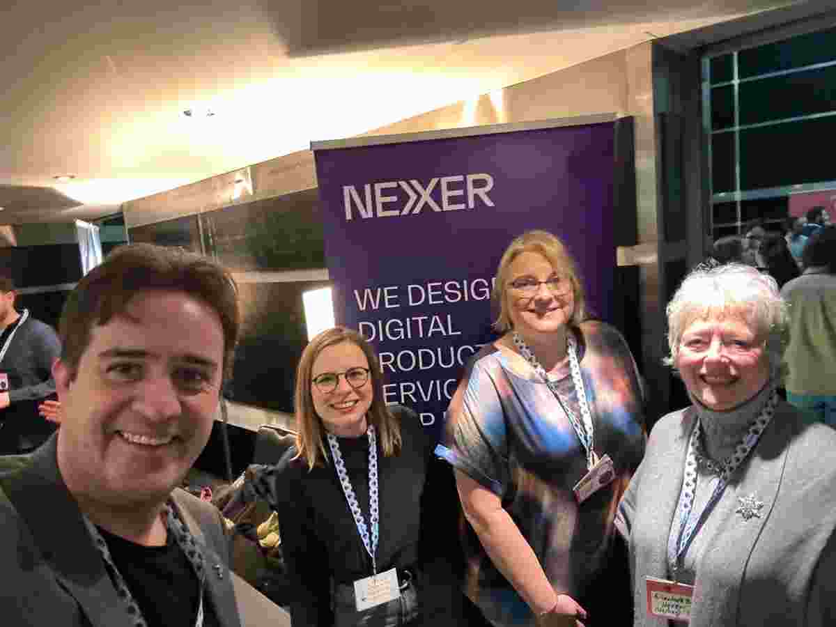 Chris, Burcu, Rachel and Elizabeth smile at the camera in front of a Nexer Digital banner