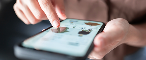 A set of hands typing on a touchscreen mobile screen. Onscreen items in an eCommerce store are visible, though out of focus.