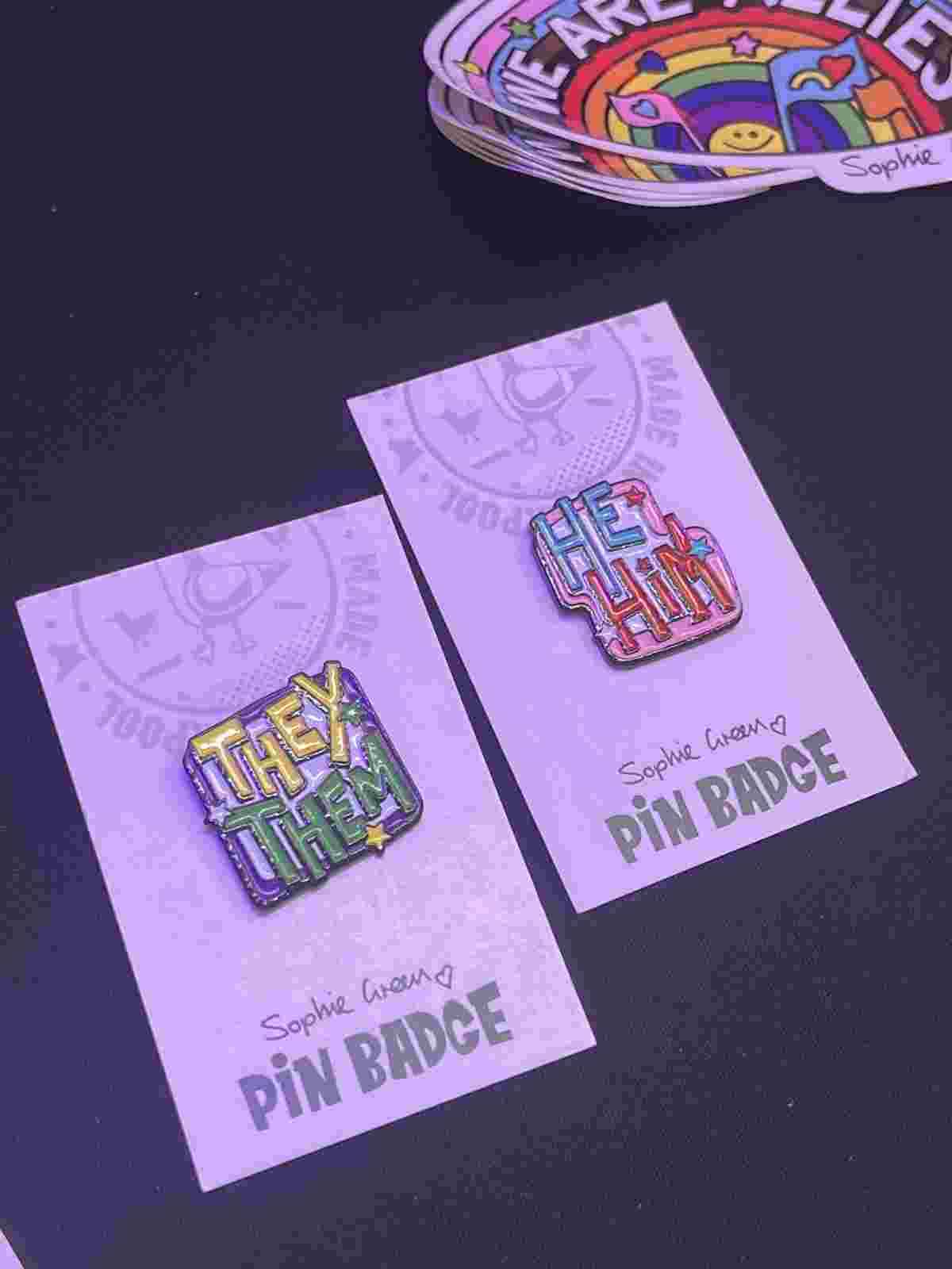 Meal pin badges showing the pronouns They/Them and He/Him