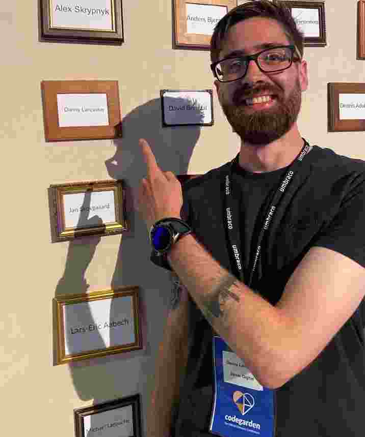 Danny standing and pointing at his name on the Umbraco MVP wall