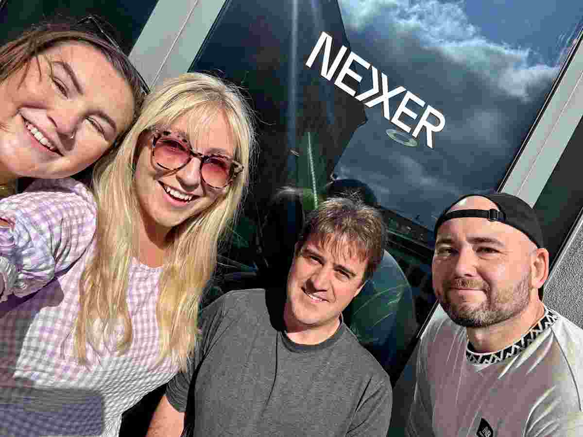 Molly, Amy, Chris and Shaun smile at the camera, taking a selfie in front of a Nexer logo