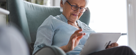 An elderly person smiles while using a tablet 