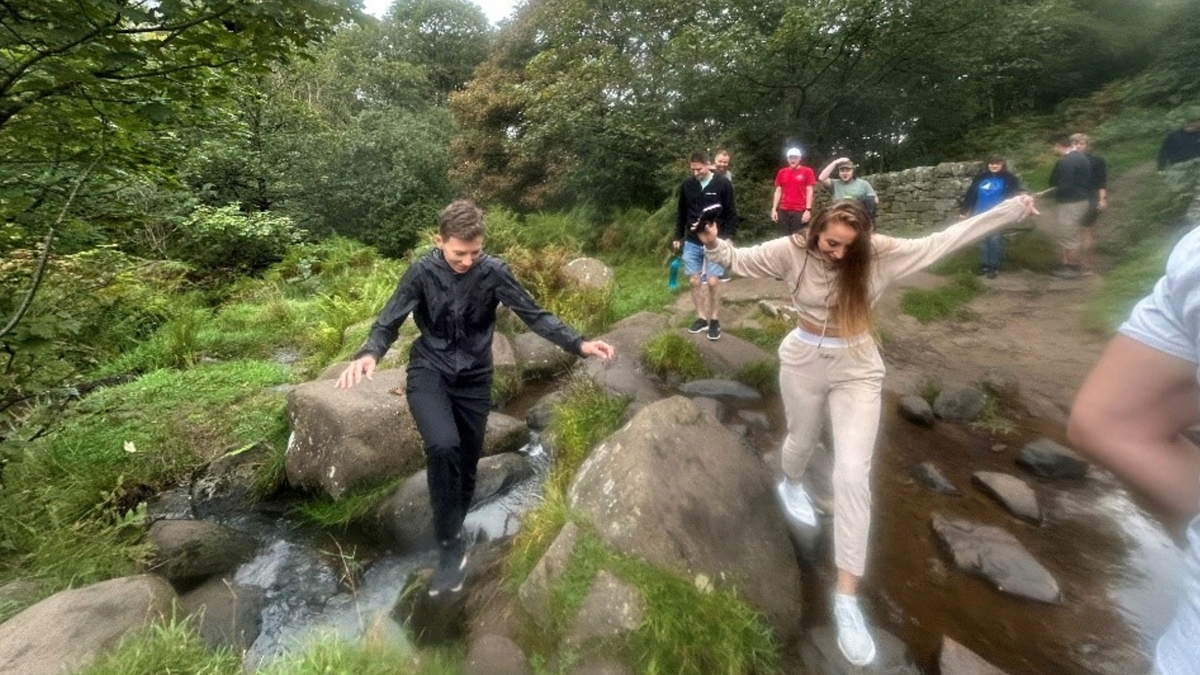 A photo of Delia jumping over some stepping stones on a river