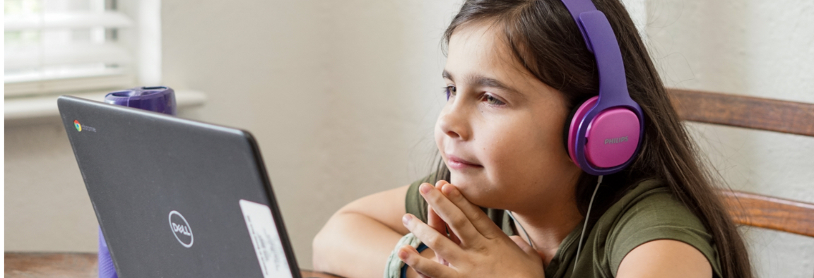 a girl is looking at a laptop screen, her face is visible, she is wearing pink and purple coloured headphones