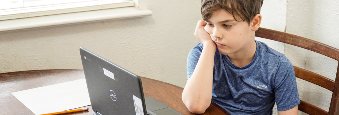 A boy looking at a laptop screen with his head resting on his chin